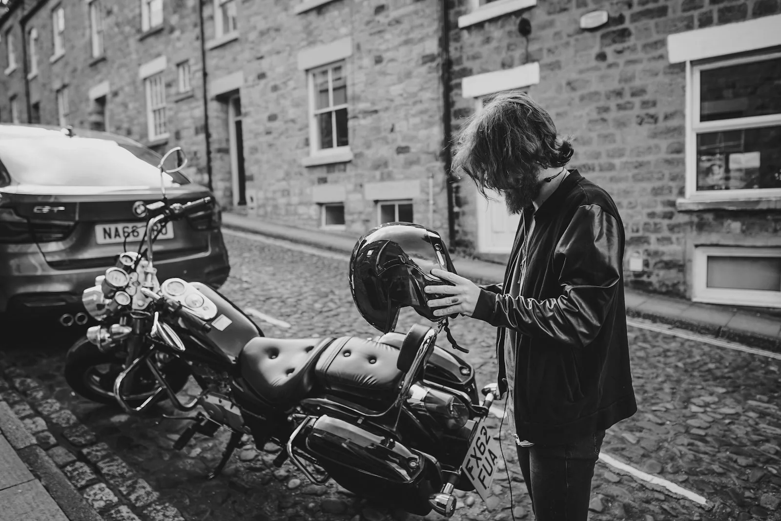 grayscale photo of man holding helmet standing near cruiser motorcycle