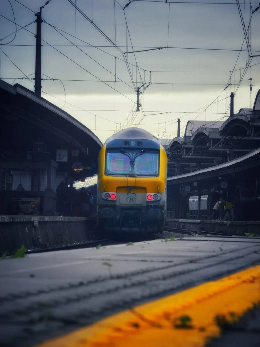 A yellow train traveling down train tracks next to a train station