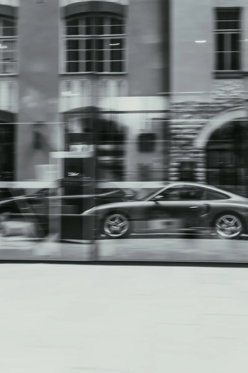 a black and white photo of a car passing by a building