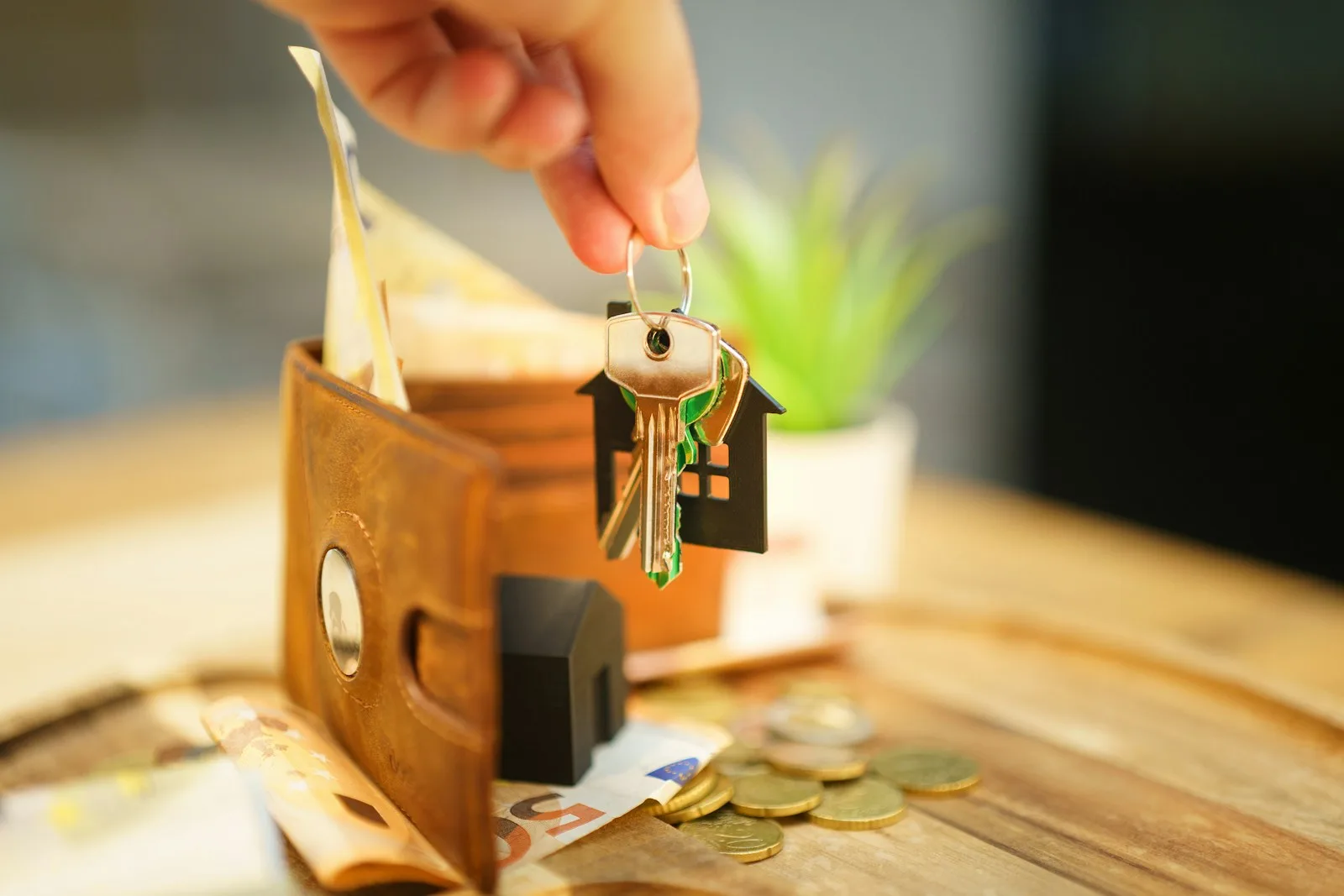 Hand holding keys with house charm and wallet.