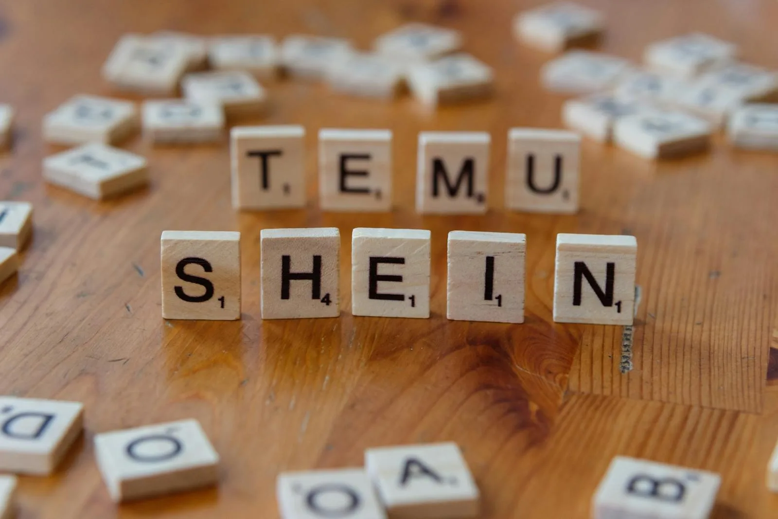 Scrabble tiles spelling 'TEMU SHEIN' on a wooden table, representing fashion brands.