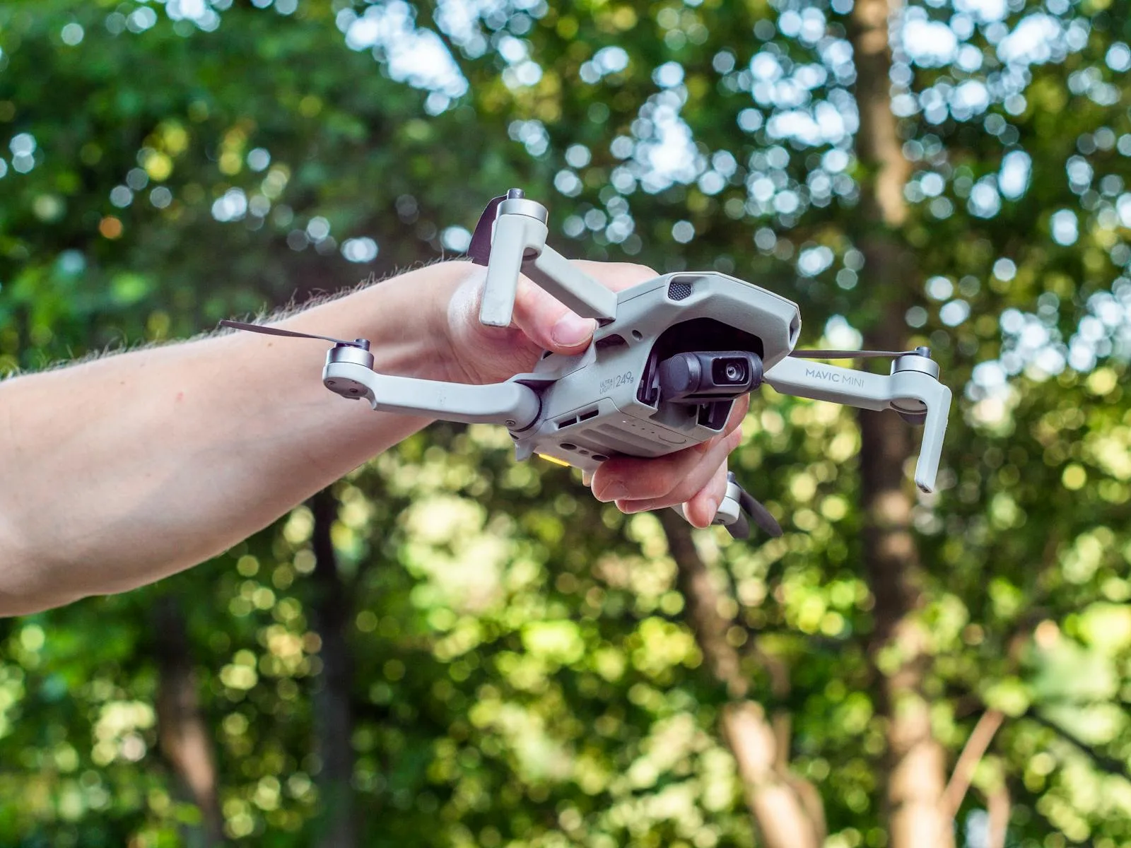 A hand holds a drone ready for flight in a lush forest environment, showcasing modern technology.