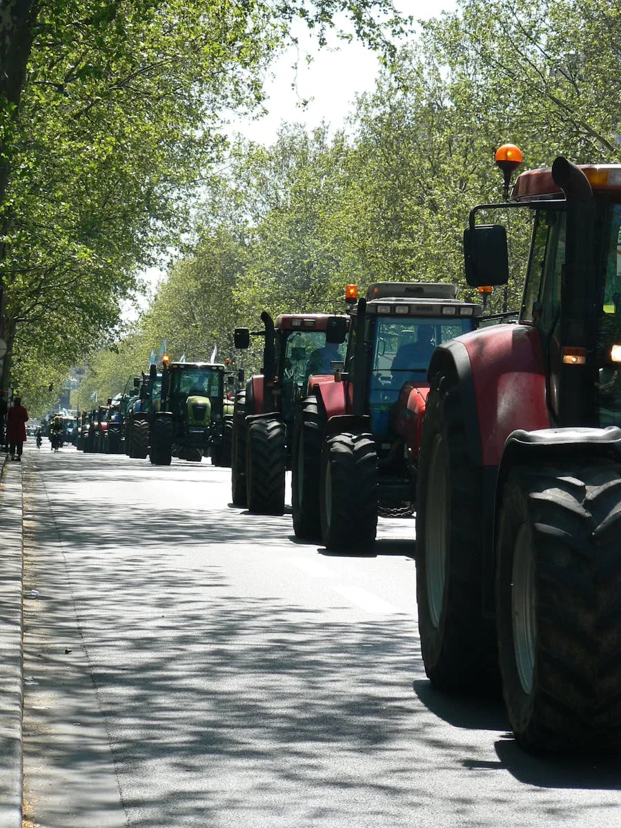 A line of tractors driving on a tree-lined street in Paris, France.