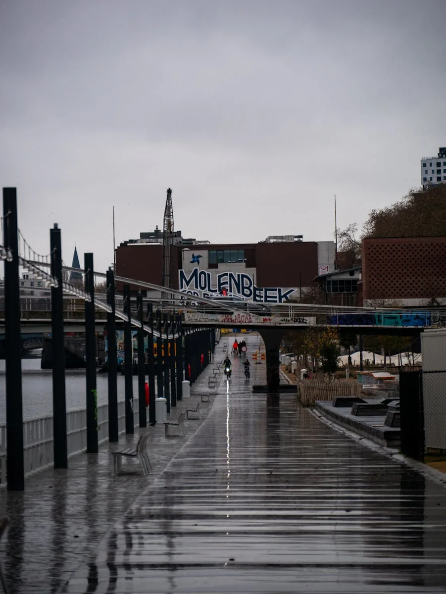 A rainy, reflective street scene captures urban life in Molenbeek, with distant cyclists.