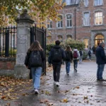 Uczniowie z plecakami wchodzą przez bramę szkoły średniej z cegły w jesienny poranek, widziani z tyłu