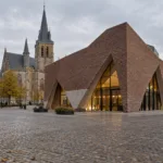 Nowoczesna hala z cegły z trójkątnymi otworami na rynku flamandzkiego miasteczka