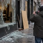 Sprzedawca fotografuje rozbitą witrynę sklepu po zamieszkach