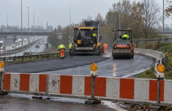 Zamknięty wjazd na obwodnicę pod Gandawą, biało-czerwone zapory i maszyny kładące nowy asfalt w pochmurny październikowy dzień