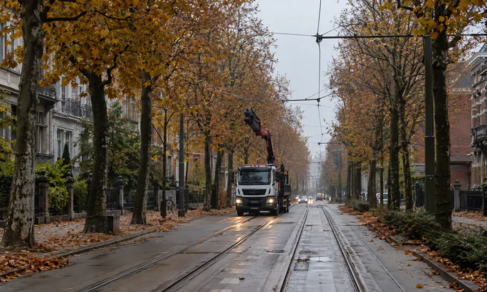 Aleja z torami tramwajowymi i siecią trakcyjną w Gandawie jesienią, w oddali ciężarówka z podniesionym żurawiem