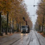 Aleja z torami tramwajowymi i siecią trakcyjną w Gandawie jesienią, w oddali ciężarówka z podniesionym żurawiem