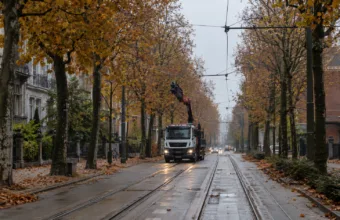 Aleja z torami tramwajowymi i siecią trakcyjną w Gandawie jesienią, w oddali ciężarówka z podniesionym żurawiem
