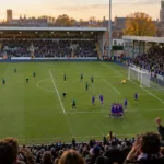 Piłkarze w fioletowych koszulkach cieszą się z gola na stadionie w Brugii, widok z trybun