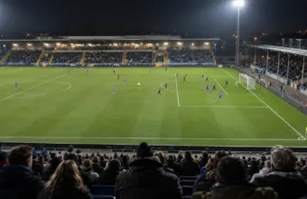 Mecz piłkarski na niewielkim stadionie przy sztucznym oświetleniu, widok z trybun