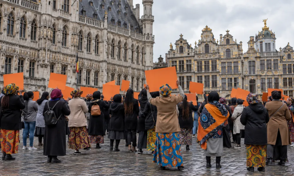 Grupa kobiet z pomarańczowymi transparentami podczas manifestacji na placu w Brukseli