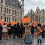 Grupa kobiet z pomarańczowymi transparentami podczas manifestacji na placu w Brukseli