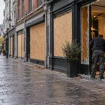 Zabite deskami witryny sklepów na deptaku w centrum Liège, sprzedawca zamiata szkło przed sklepem - wizualizacja