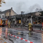 Spalony budynek supermarketu i wozy strażackie na ulicy we flamandzkim mieście - wizualizacja