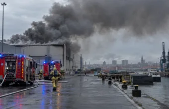 Gęsty dym nad halą przemysłową w porcie, wozy strażackie na nabrzeżu