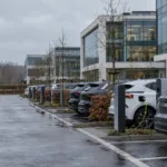Parking przy biurowcu pod Brukselą z rzędami samochodów elektrycznych i hybrydowych podłączonych do ładowarek
