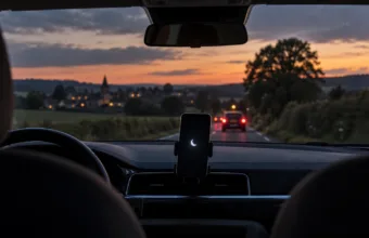 Wnętrze samochodu o zmierzchu, smartfon w uchwycie na desce rozdzielczej z symbolem trybu „Nie przeszkadzać”, przed autem wiejska droga w Walonii