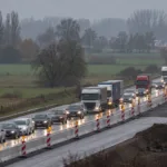 Korek samochodów i ciężarówek na autostradzie zwężonej przez roboty drogowe, pachołki i bariery wśród jesiennych pól