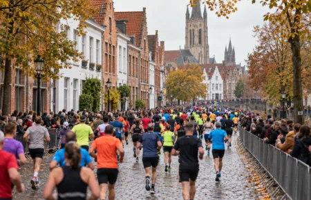 Biegacze półmaratonu widziani od tyłu na ulicy w centrum flamandzkiego miasta, wzdłuż trasy kibice