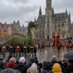 Parada z figurą zielonego smoka na rynku przed gotyckim ratuszem, tłum widzów z parasolami