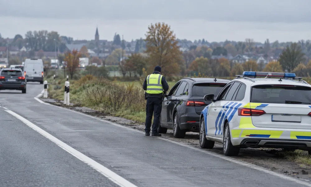 Policjant w odblaskowej kamizelce przy zatrzymanym samochodzie na poboczu drogi, obok radiowóz belgijskiej policji