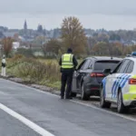 Policjant w odblaskowej kamizelce przy zatrzymanym samochodzie na poboczu drogi, obok radiowóz belgijskiej policji