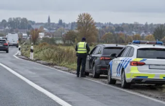 Policjant w odblaskowej kamizelce przy zatrzymanym samochodzie na poboczu drogi, obok radiowóz belgijskiej policji