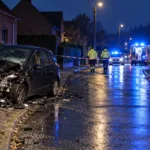 Rozbity samochód przy słupie energetycznym i uszkodzone zaparkowane auta na ulicy we Flandrii nocą (wizualizacja SI)