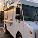Biały food truck na parkingu z laptopem i wydrukiem umowy na masce