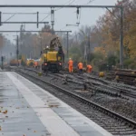 Robotnicy w kamizelkach odblaskowych wymieniają szyny przy pustym peronie małej stacji kolejowej jesienią