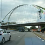 Nowy stalowy most łukowy z malowidłem kwiatów nad autostradą E40 w Bertem, widziany z jezdni, pod mostem ruch samochodów