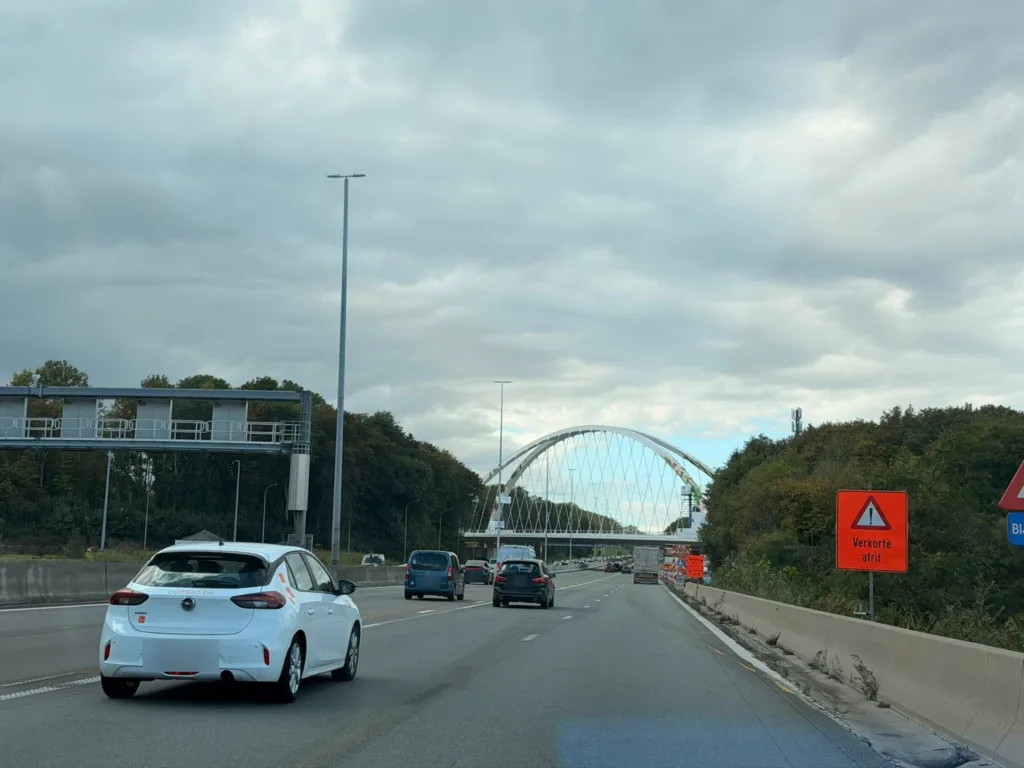 Widok z autostrady E40 na nowy most łukowy w Bertem, z prawej pomarańczowa tablica Verkorte afrit