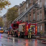 Wóz strażacki z podnośnikiem przed ceglaną kamienicą z okopconym oknem na bulwarze w Brukseli