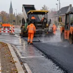 Układanie nowego asfaltu na skrzyżowaniu we flamandzkim mieście, walec i rozściełacz