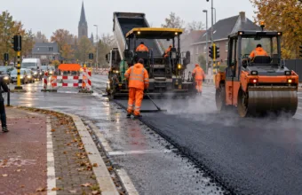 Układanie nowego asfaltu na skrzyżowaniu we flamandzkim mieście, walec i rozściełacz
